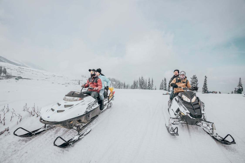 Four people riding two snowmobiles
